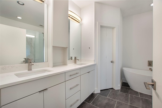 full bath with a sink, a freestanding bath, double vanity, and tile patterned flooring