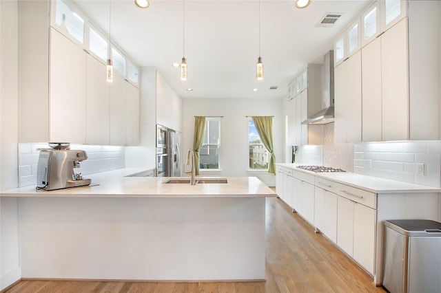 kitchen with visible vents, a sink, appliances with stainless steel finishes, wall chimney range hood, and light wood-type flooring