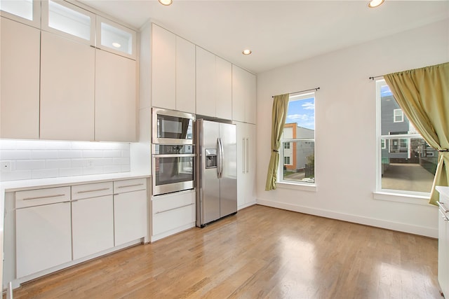 kitchen with decorative backsplash, stainless steel appliances, light countertops, and light wood-style floors