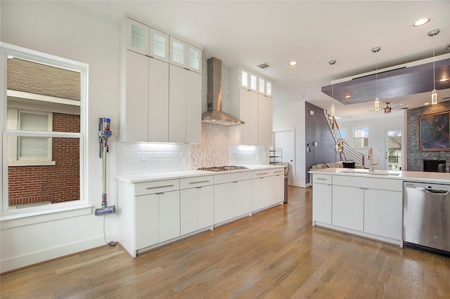 kitchen with tasteful backsplash, wall chimney range hood, open floor plan, stainless steel appliances, and a sink