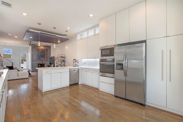 kitchen with visible vents, a peninsula, stainless steel appliances, open floor plan, and a large fireplace