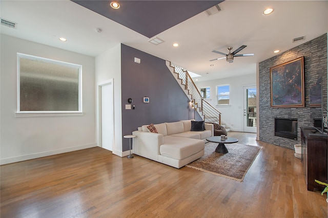 living room with visible vents, a stone fireplace, wood finished floors, and stairs