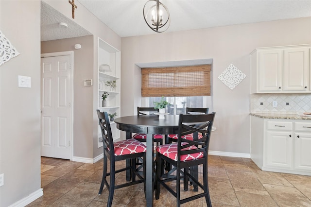 dining room featuring a chandelier, baseboards, a textured ceiling, and stone tile flooring