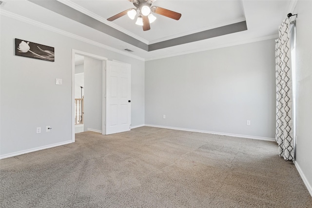 carpeted spare room featuring baseboards, a raised ceiling, ornamental molding, and a ceiling fan