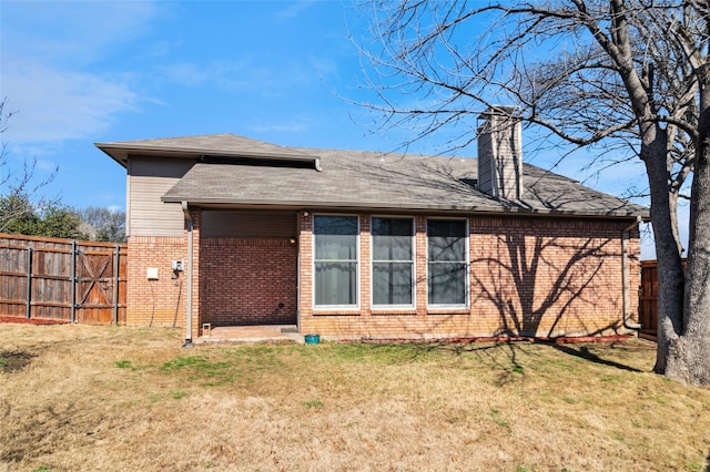 rear view of property with fence, brick siding, and a lawn