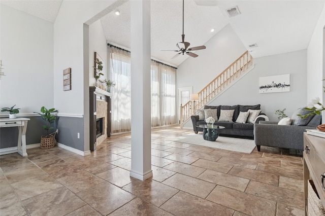 living area with visible vents, high vaulted ceiling, a ceiling fan, a fireplace, and stairs