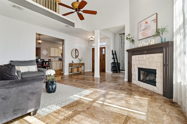 living area with visible vents, ceiling fan, baseboards, a fireplace, and a high ceiling