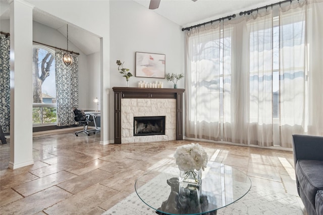 living area featuring a tiled fireplace, ceiling fan with notable chandelier, baseboards, and lofted ceiling