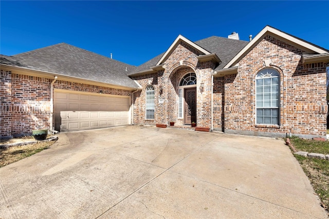 view of front of home with roof with shingles, concrete driveway, a garage, brick siding, and a chimney