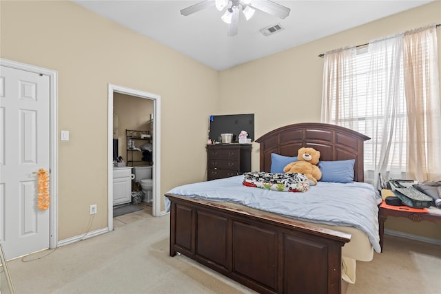 bedroom with visible vents, connected bathroom, baseboards, light colored carpet, and ceiling fan