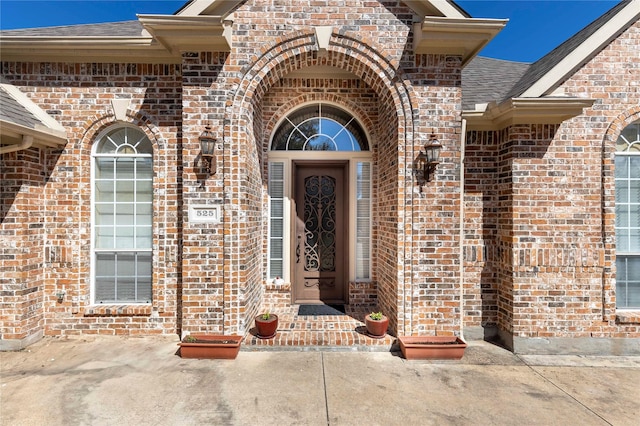 entrance to property featuring brick siding and a shingled roof