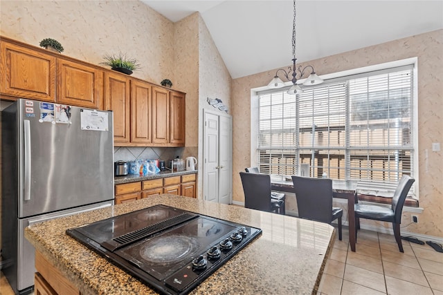 kitchen featuring brown cabinetry, wallpapered walls, lofted ceiling, freestanding refrigerator, and black electric stovetop