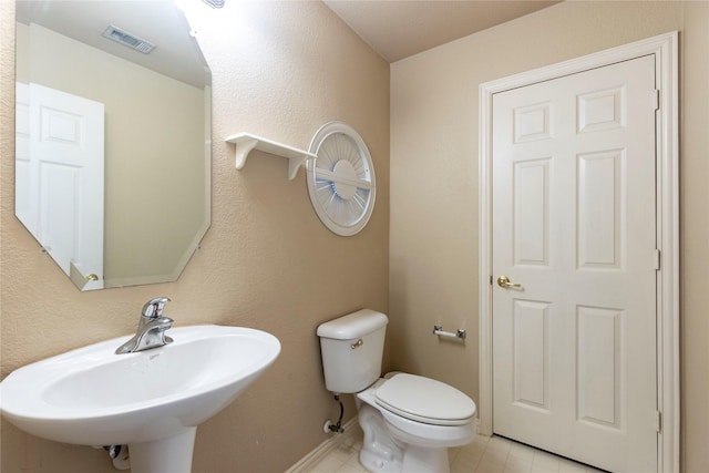 half bathroom with tile patterned floors, visible vents, toilet, a sink, and baseboards