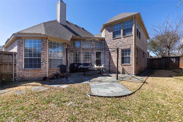 back of house with a patio, a fenced backyard, a chimney, a lawn, and brick siding