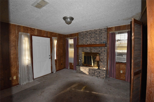 unfurnished living room featuring visible vents, a textured ceiling, wooden walls, carpet flooring, and a brick fireplace