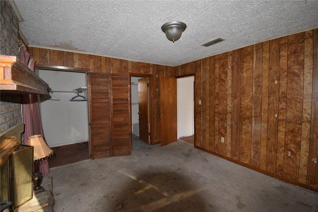 unfurnished bedroom featuring visible vents, carpet floors, a textured ceiling, and wood walls