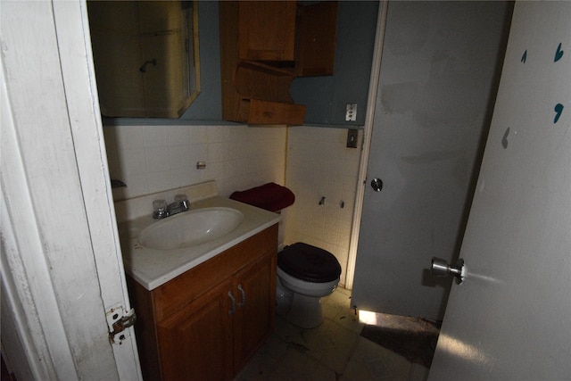 half bath with vanity, tile walls, toilet, and a wainscoted wall