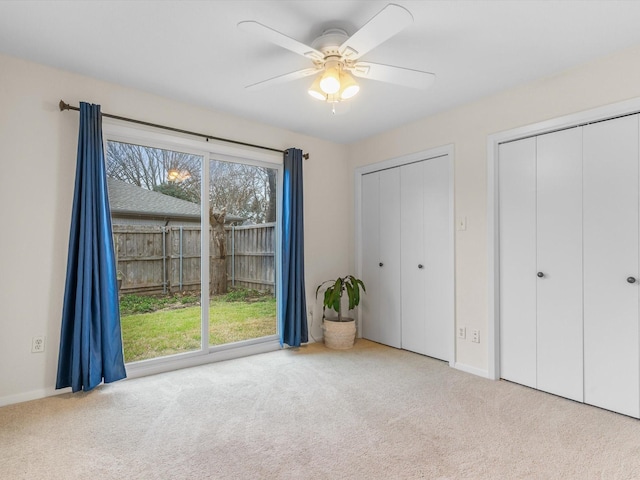 unfurnished bedroom with carpet flooring, a ceiling fan, multiple closets, and baseboards