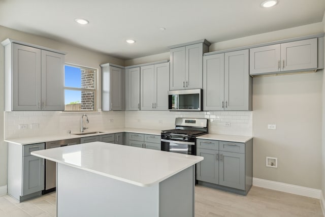 kitchen with gray cabinetry, a sink, backsplash, stainless steel appliances, and light countertops