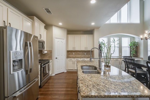 kitchen featuring visible vents, a sink, stainless steel appliances, white cabinetry, and a kitchen island with sink