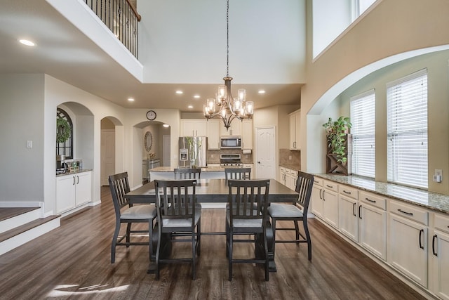 dining area with baseboards, a high ceiling, recessed lighting, dark wood-type flooring, and a notable chandelier