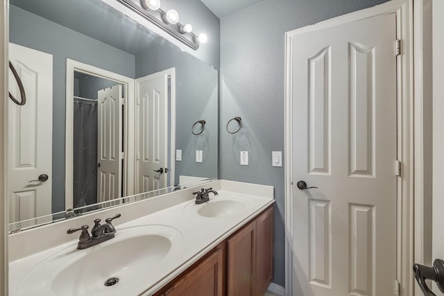 full bath featuring a sink, double vanity, and a textured wall