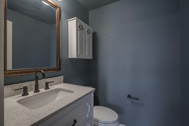 half bathroom with vanity, toilet, and a textured wall