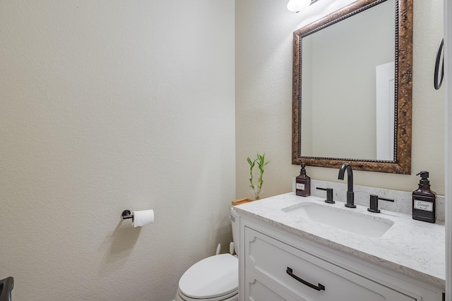 bathroom with toilet, vanity, and a textured wall