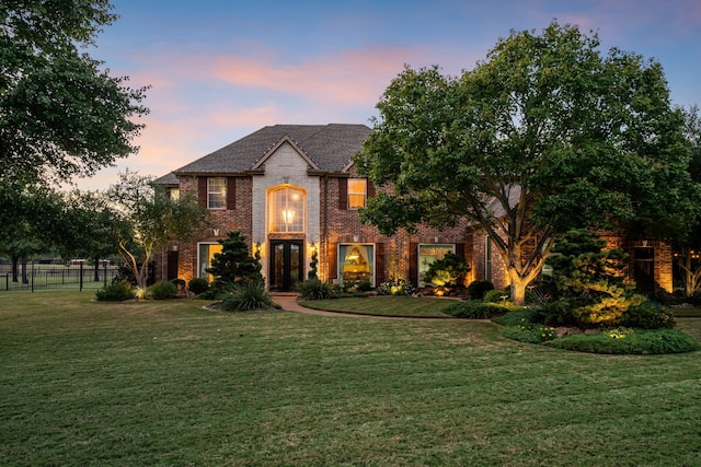 french country style house with a front lawn, fence, and brick siding