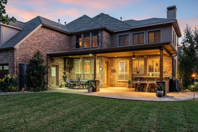 rear view of property featuring a yard, brick siding, and a ceiling fan