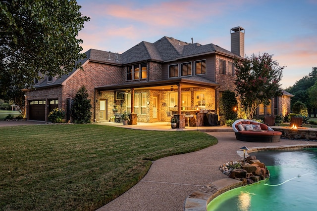 back of property at dusk with a yard, a fire pit, brick siding, a chimney, and a patio area