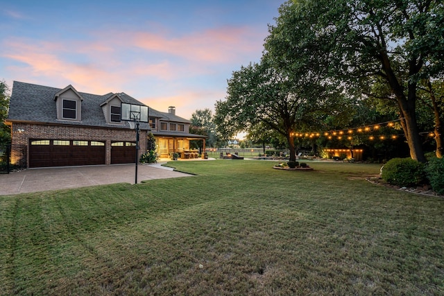 yard at dusk with an attached garage, concrete driveway, and fence