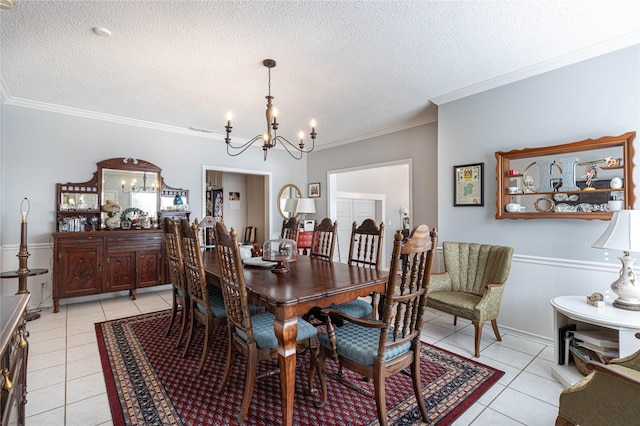 dining space with ornamental molding, a textured ceiling, wainscoting, light tile patterned floors, and a chandelier