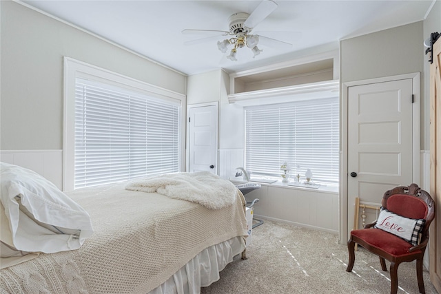 carpeted bedroom with a ceiling fan and a wainscoted wall