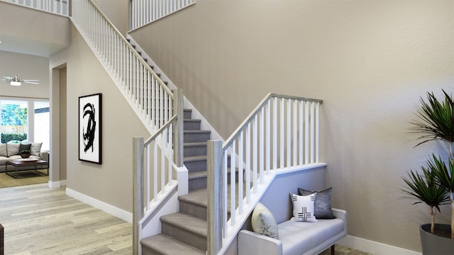 stairs with a ceiling fan, a high ceiling, baseboards, and wood finished floors