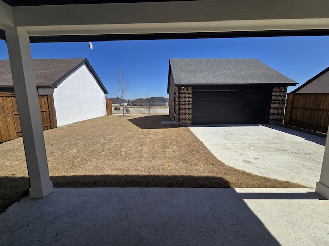 view of yard featuring an outdoor structure, concrete driveway, fence, and a garage