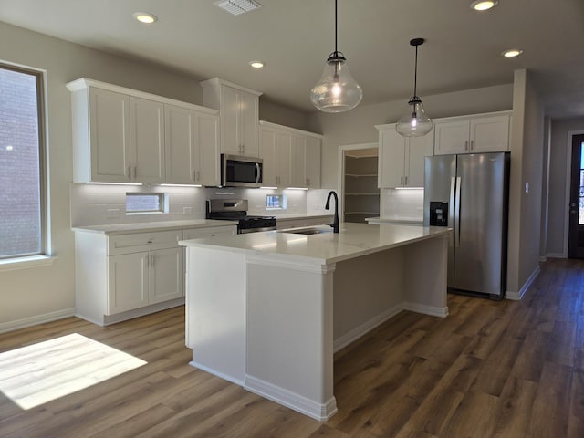 kitchen with a center island with sink, wood finished floors, white cabinets, stainless steel appliances, and a sink