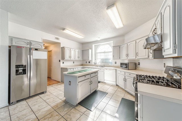 kitchen with under cabinet range hood, light countertops, light tile patterned floors, stainless steel appliances, and a sink