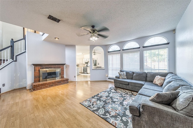 living room featuring a ceiling fan, wood finished floors, visible vents, a textured ceiling, and a brick fireplace