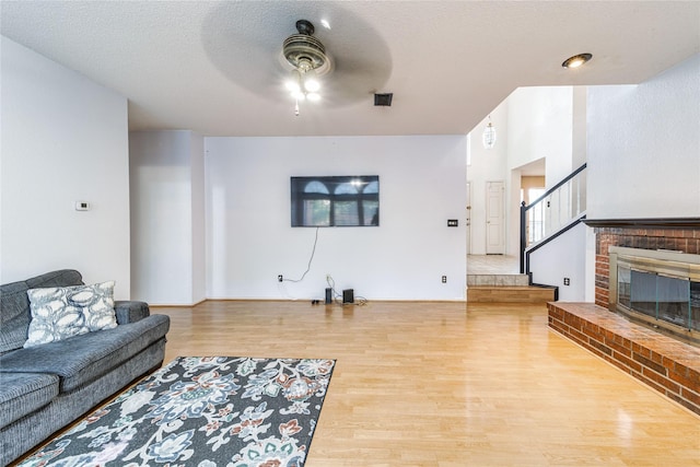 living room featuring a ceiling fan, a textured ceiling, wood finished floors, stairway, and a brick fireplace