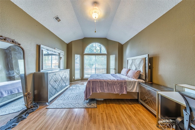 bedroom featuring visible vents, lofted ceiling, light wood-style floors, and a textured wall