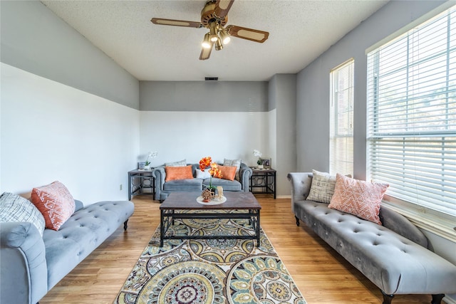 living area featuring light wood finished floors, visible vents, a textured ceiling, and ceiling fan