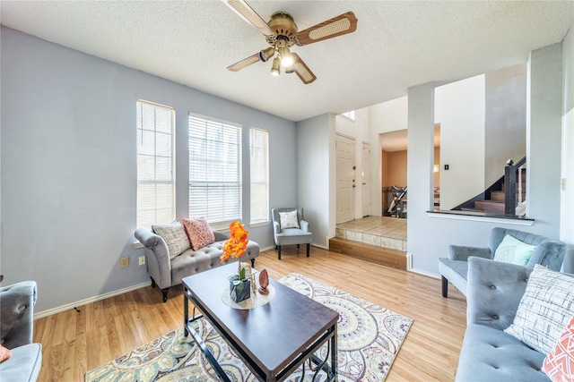 living room with a textured ceiling, wood finished floors, stairway, baseboards, and ceiling fan