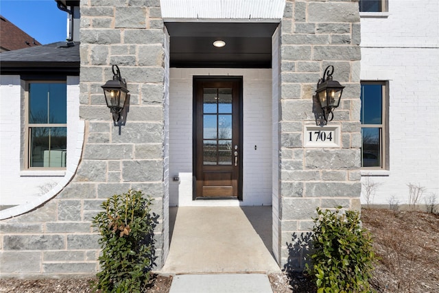 doorway to property featuring brick siding and a shingled roof