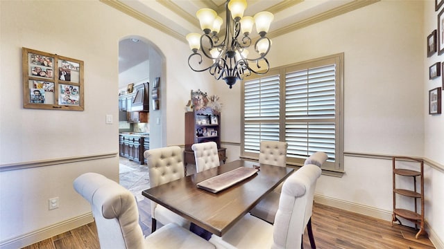 dining space featuring a tray ceiling, ornamental molding, an inviting chandelier, wood finished floors, and arched walkways