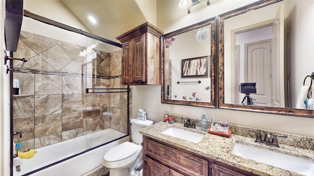 bathroom featuring double vanity, toilet, combined bath / shower with glass door, and a sink