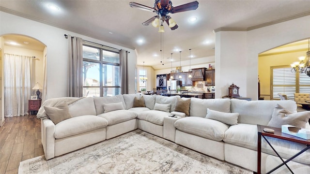 living area featuring crown molding, recessed lighting, ceiling fan with notable chandelier, wood finished floors, and arched walkways