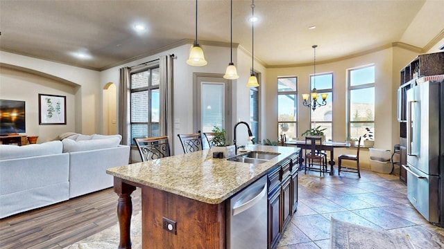 kitchen with open floor plan, light stone counters, appliances with stainless steel finishes, plenty of natural light, and a sink