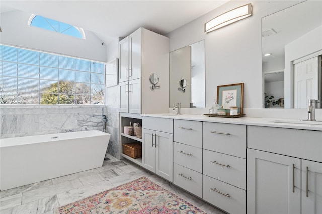 full bath with a sink, marble finish floor, a freestanding tub, and double vanity