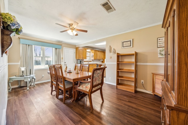 dining space with visible vents, ornamental molding, a ceiling fan, wainscoting, and dark wood-style flooring